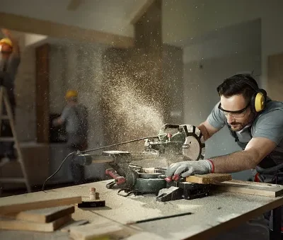 male carpenter cutting wood plank with electric saw at construction site