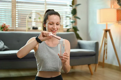 sporty woman preparing healthy supplement dissolving collagen powder in a glass of water